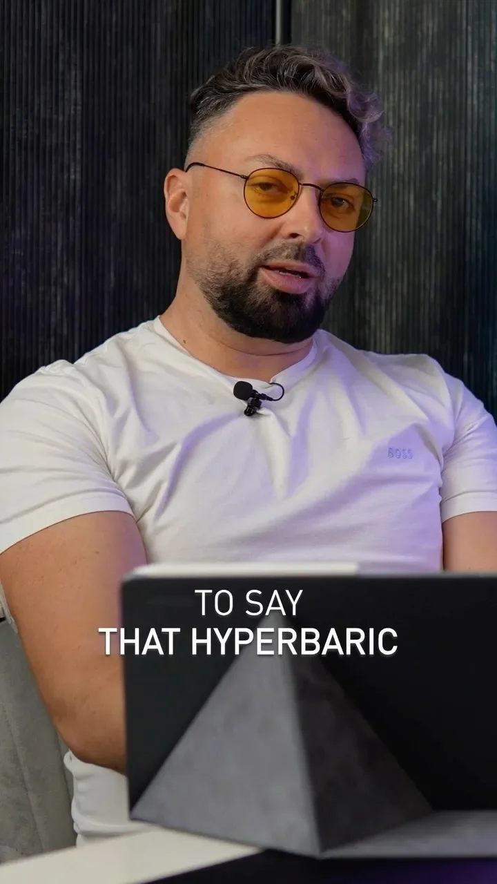 Man in a white T-shirt speaking to the camera in a studio